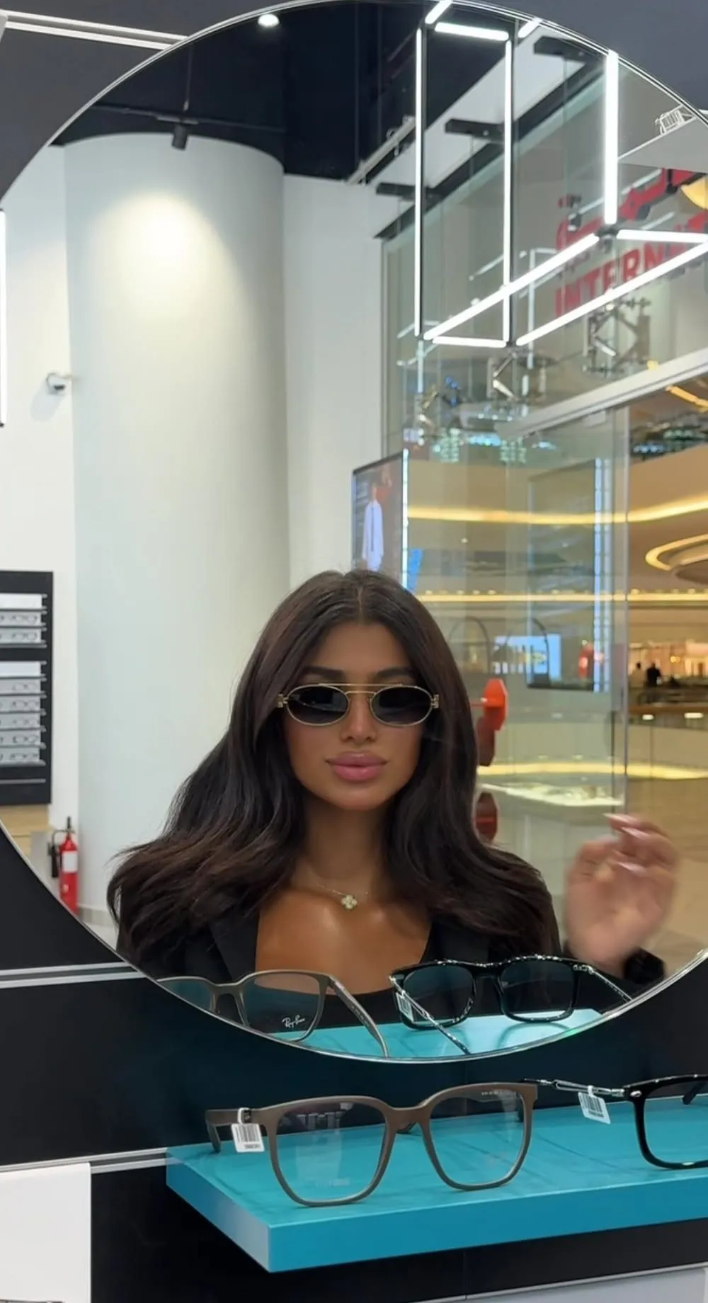 Woman in gold oval sunglasses reflected in a round store mirror